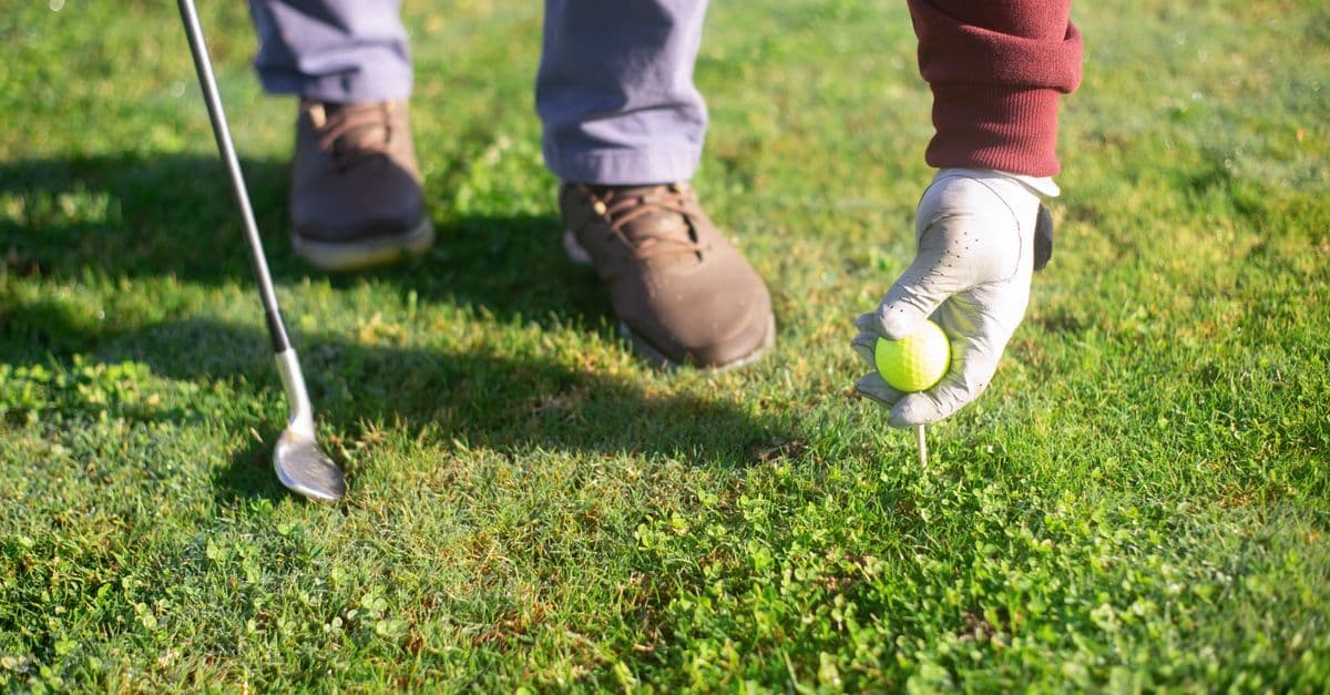 A golfer places a golf ball on a tee in a lush green field, ready to swing.