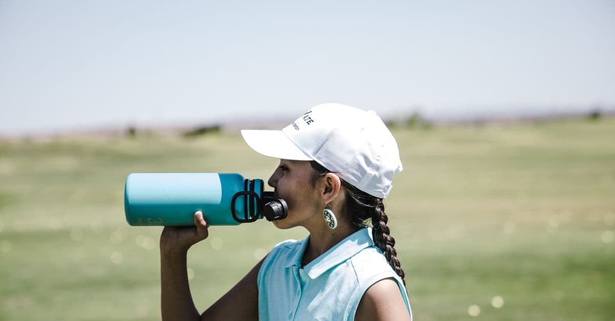 Woman golfer taking a break to hydrate on a sunny day in a field.