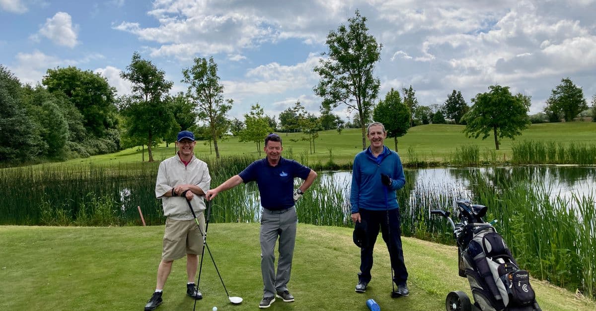 Three golfers smiling on a green Irish course with clear skies and lush surroundings.