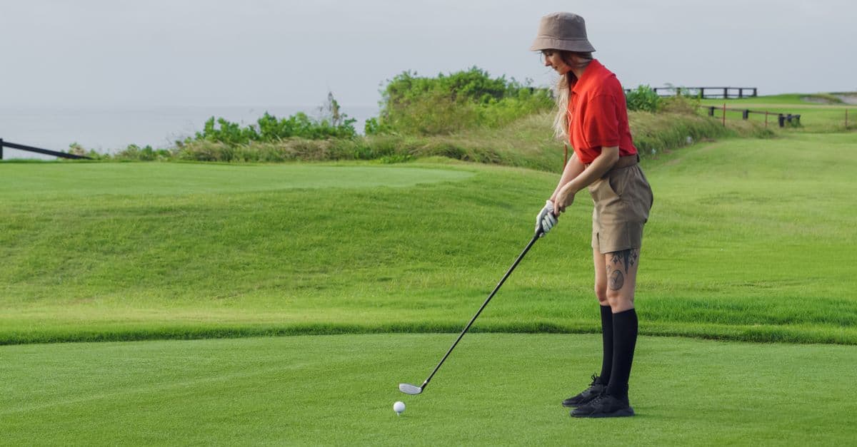 A woman golfer in red shirt on a lush golf course preparing to swing.