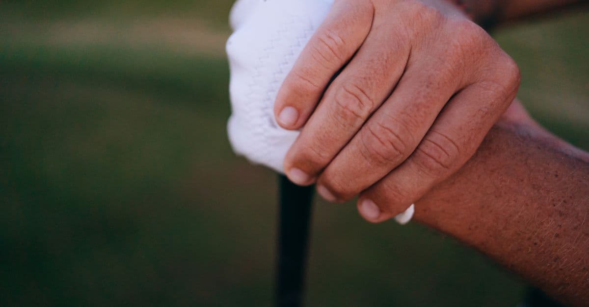 Detailed view of hands gripping a golf club with a white glove outdoors.