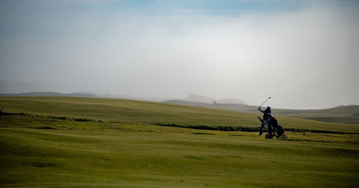 A golfer swings on a vast, misty course under a clear sky, illustrating serene sportsmanship.