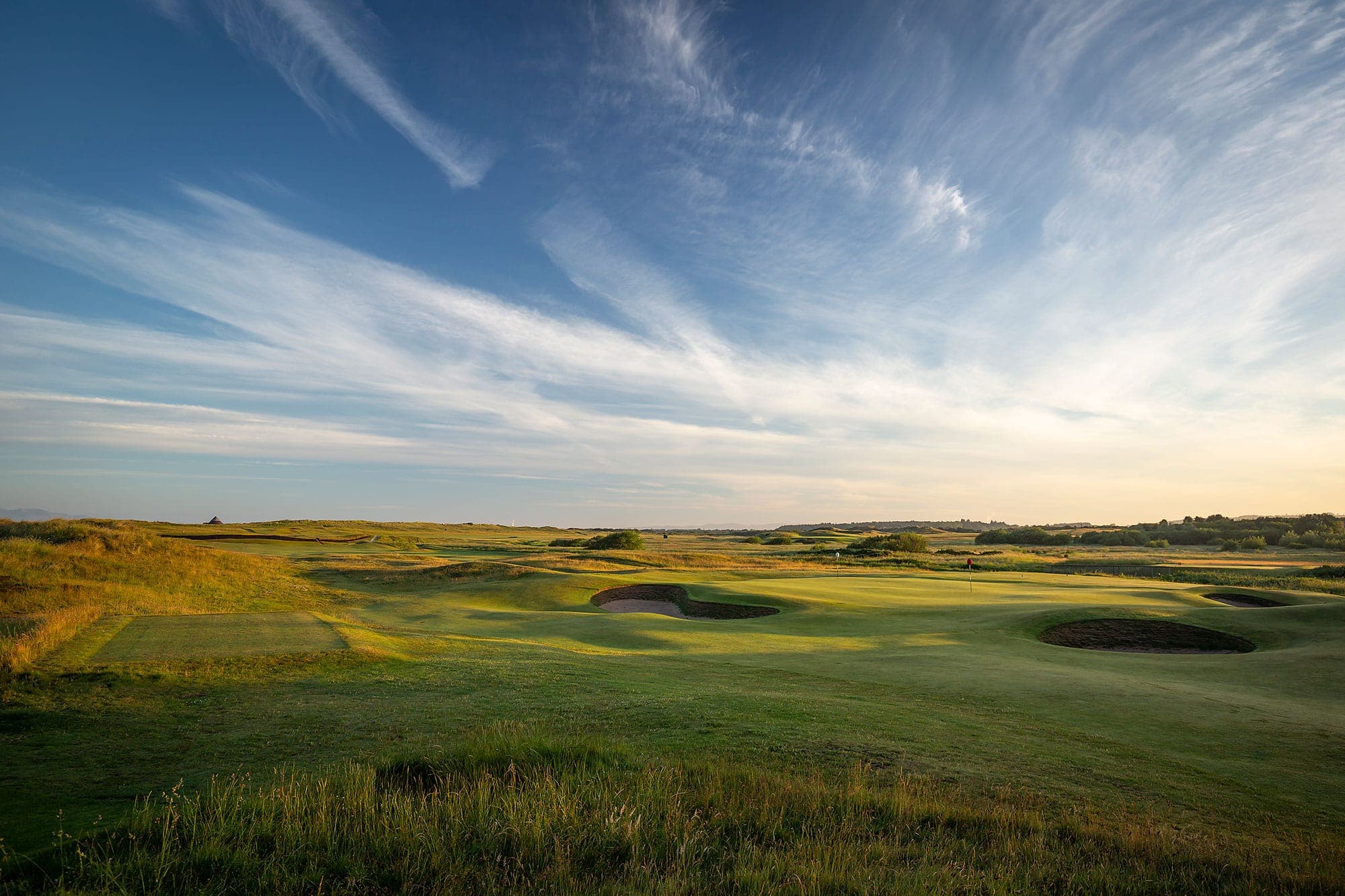 A green ringed by revetted pot bunkers amid rolling dunes and fescue on the Prestwick links under a wide Ayrshire sky.