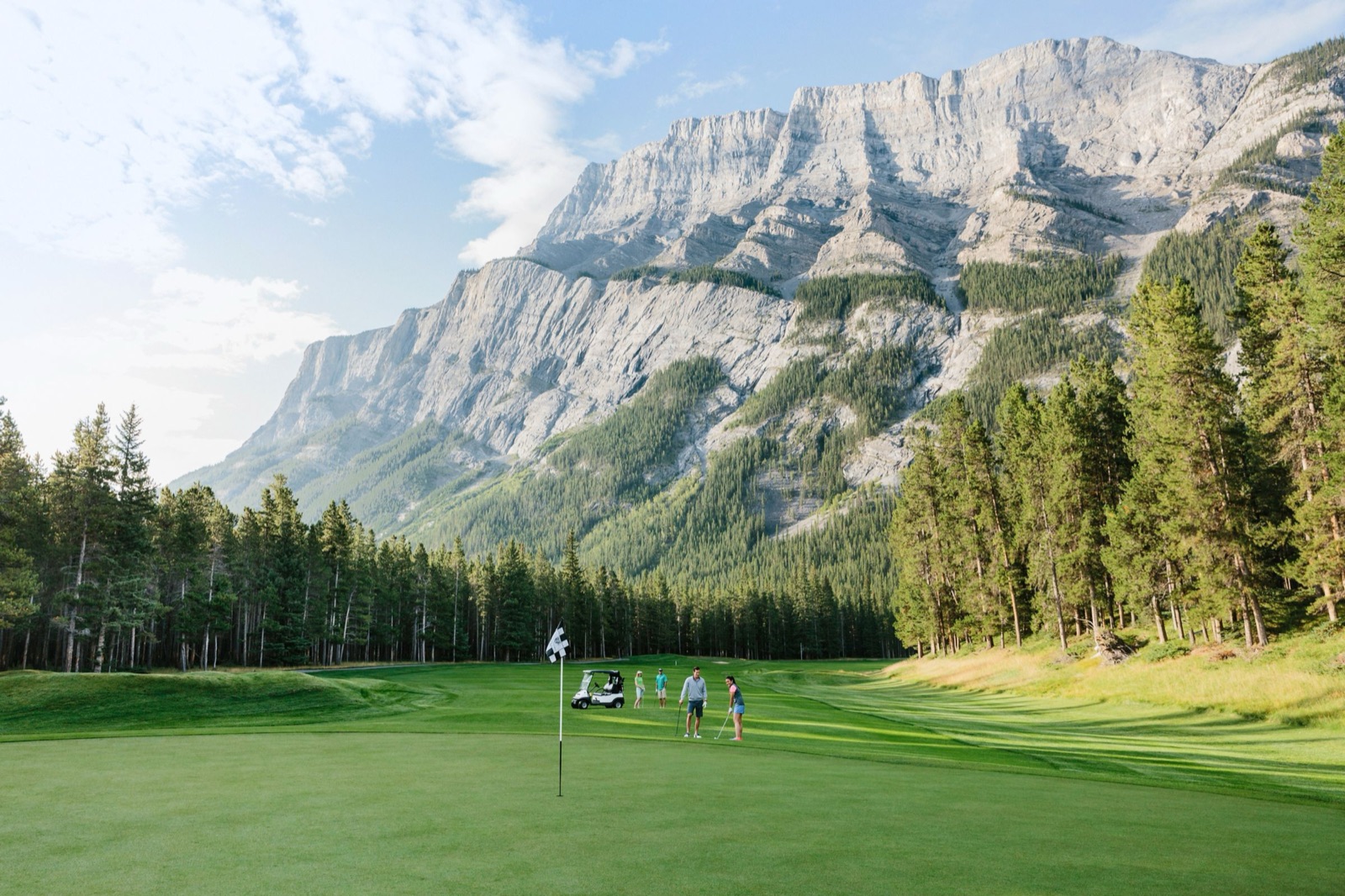 Golfers putting on a green at Fairmont Banff Springs beneath the rock face of Mount Rundle.