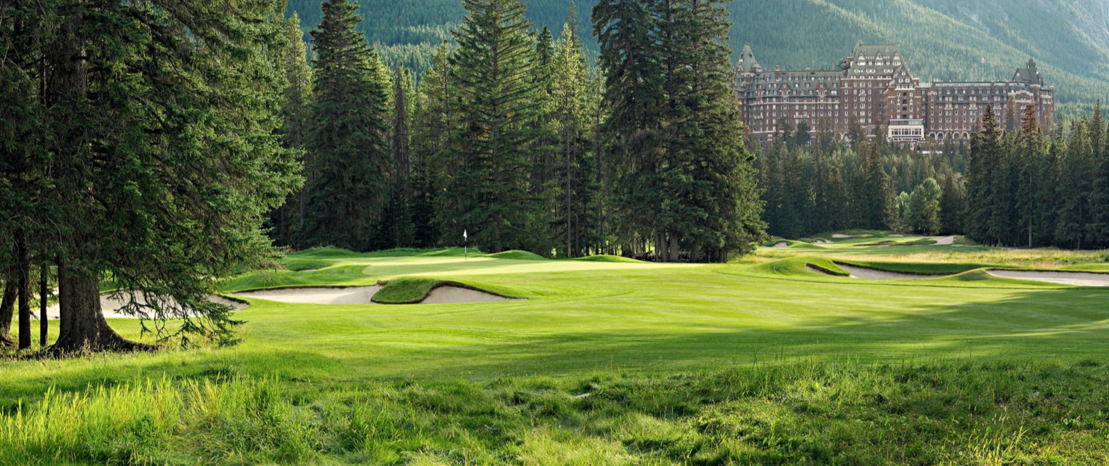 A manicured green and bunkered fairway on the Stanley Thompson course at Fairmont Banff Springs, with the hotel and Mount Rundle behind.