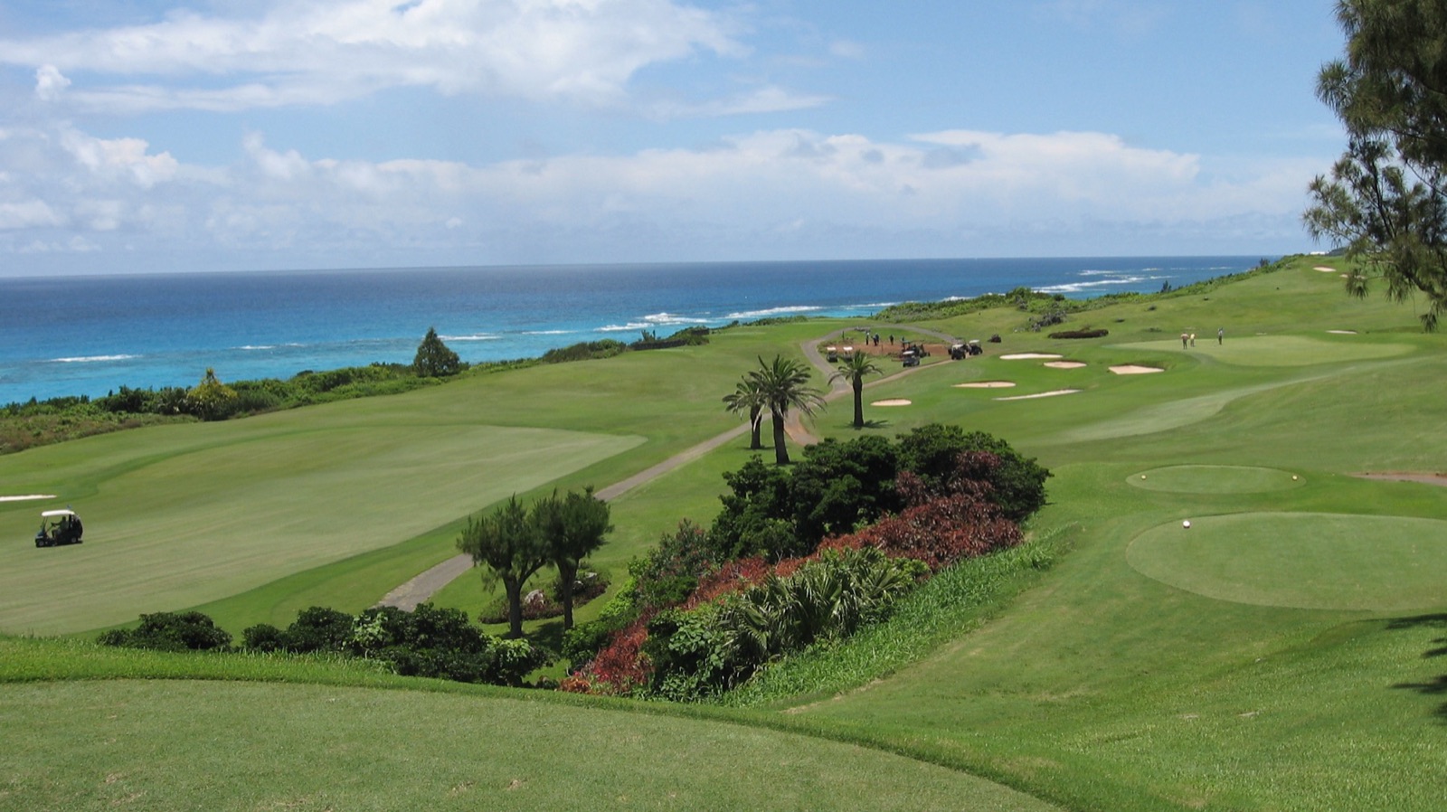Fairways falling away toward a reef line at the Mid Ocean Club, Bermuda, with surf breaking and the deep blue Atlantic beyond.