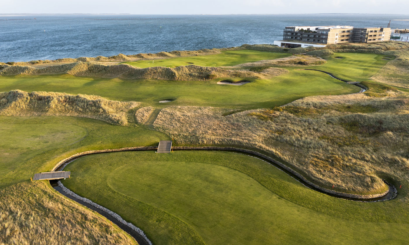 A green and fairway at Golfclub Budersand Sylt, framed by dune grasses and pot bunkers, with the North Sea behind.