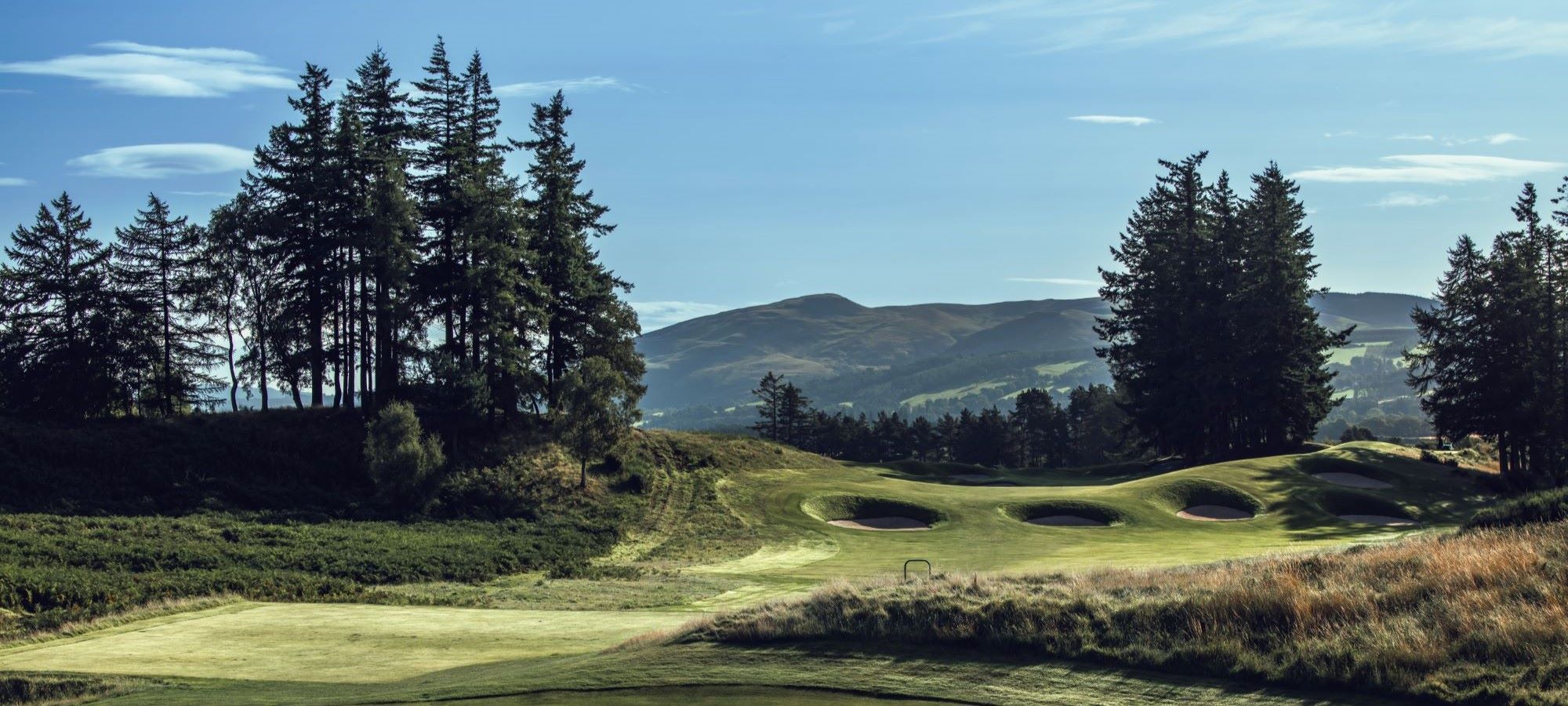 A bunkered fairway and green on the King's Course at Gleneagles, framed by Scots pines and the Perthshire hills.