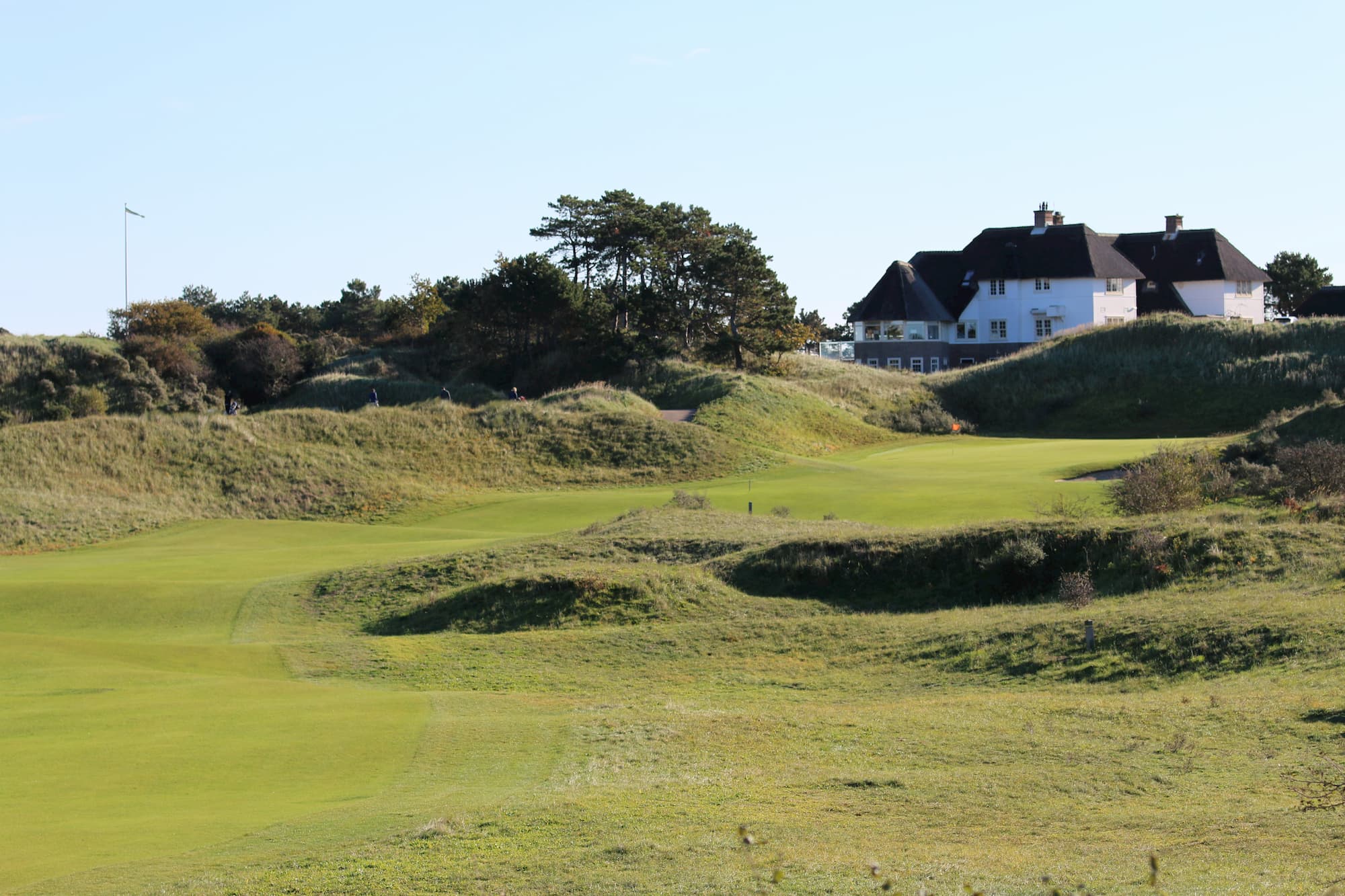 A green among the dunes with the historic thatched-roof clubhouse behind at Kennemer Golf & Country Club.