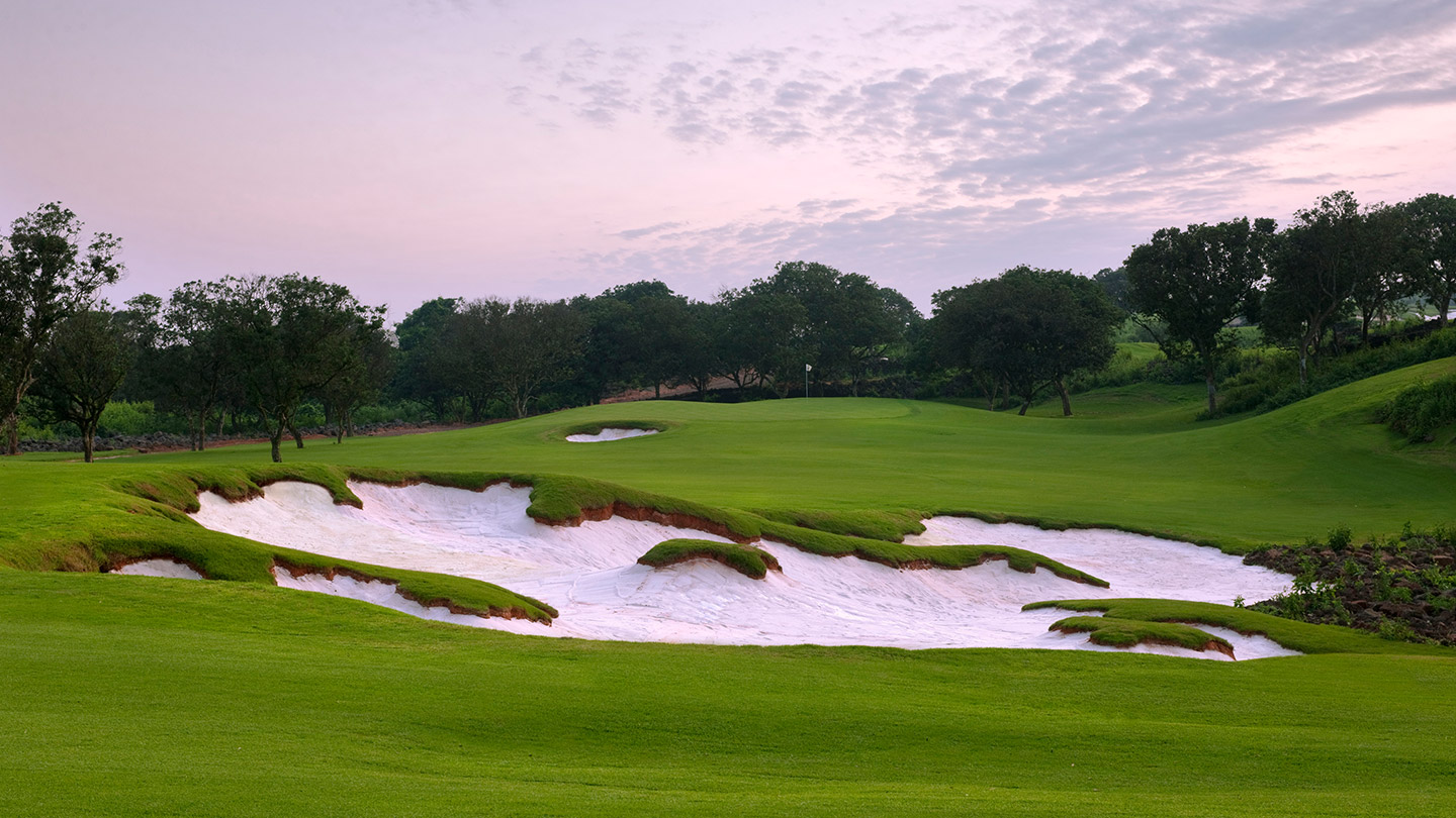 A green and sculpted white-sand bunker on the Blackstone Course at Mission Hills Haikou at dusk.