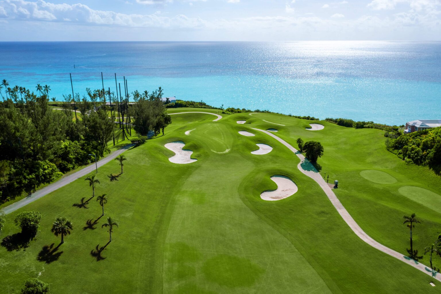 An aerial view down a wide fairway at Port Royal, stepped with kidney-shaped bunkers toward a green, palms either side and the Atlantic behind.