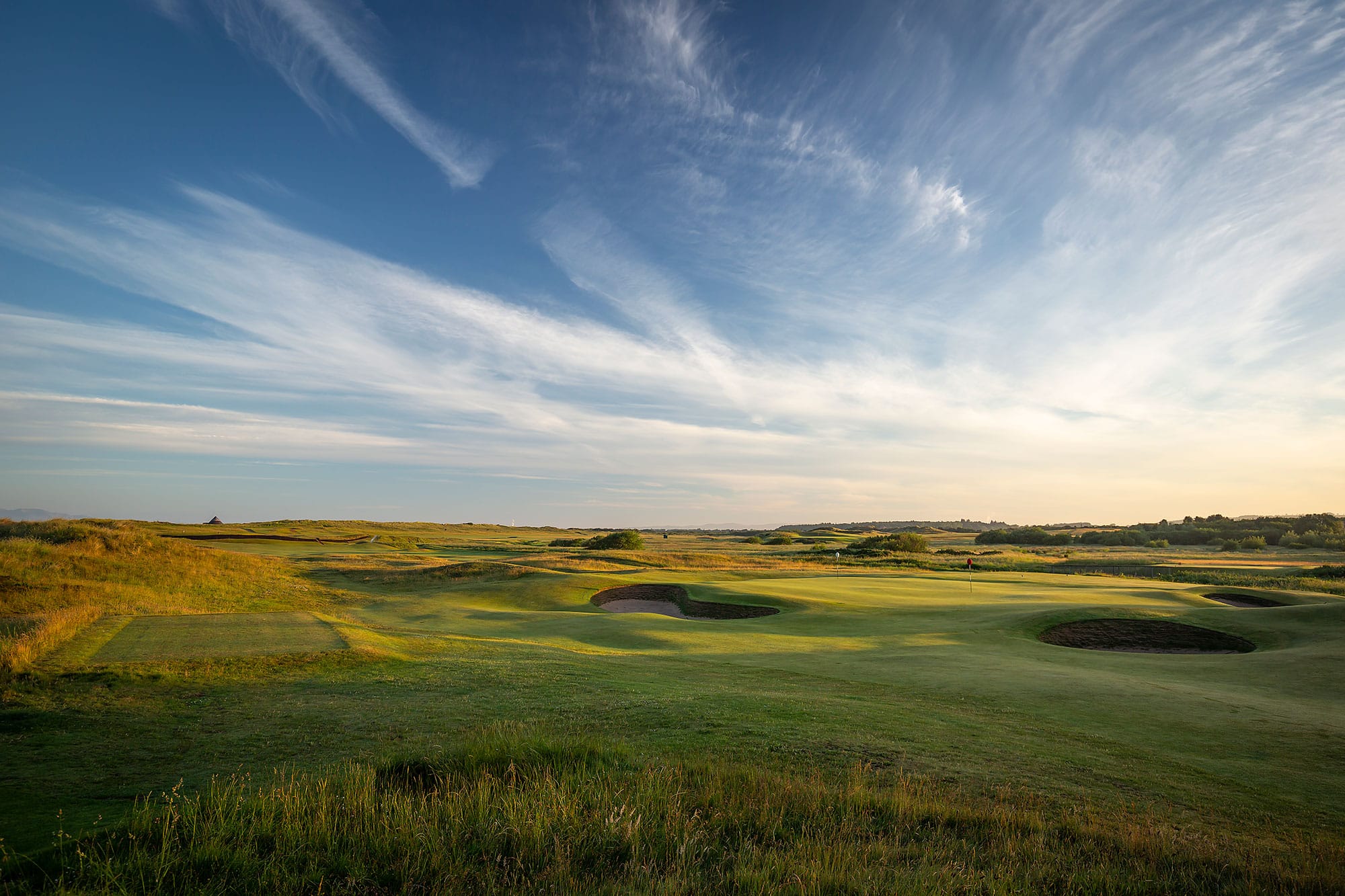 A green ringed by revetted pot bunkers amid rolling dunes and fescue on the Prestwick links under a wide Ayrshire sky.